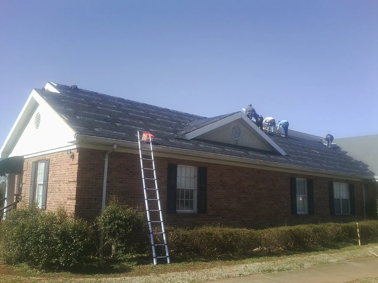 Crew tearing shingles off a brick ranch roof with a ladder set — Metal Roof Repair work by our crew in Leiters Ford