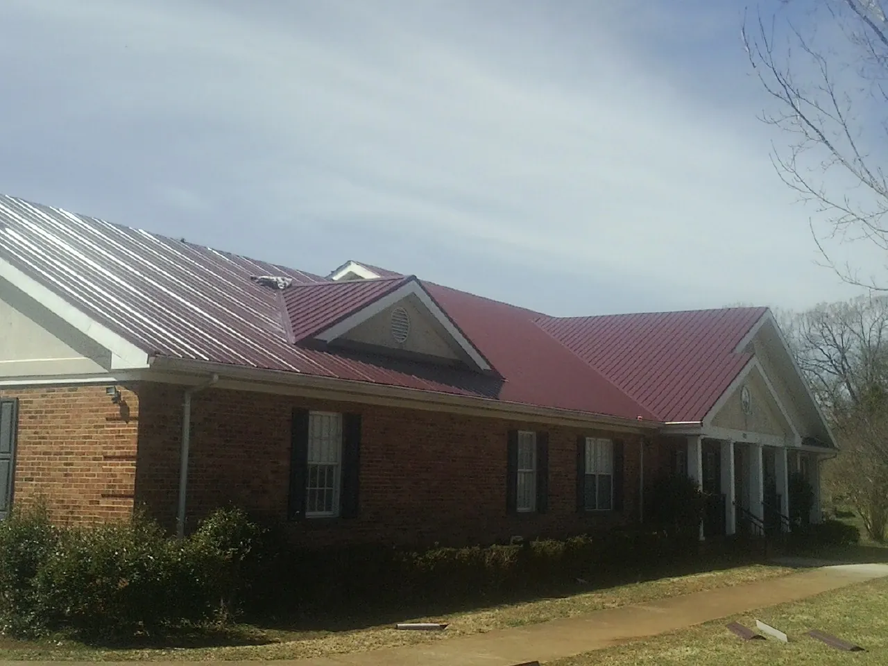 Red metal roof with gabled entries on a long brick building, from a Hail Damage Roof Repair job in Leiters Ford