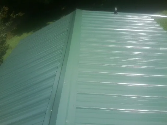New green metal panels meeting at the ridge of a roof — Flat Roof Repair work by our crew in Leiters Ford