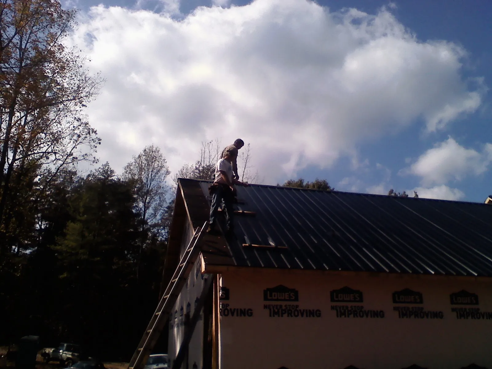 Roofer fastening dark metal panels high against a cloudy sky, from a Roof Inspection job in Leiters Ford