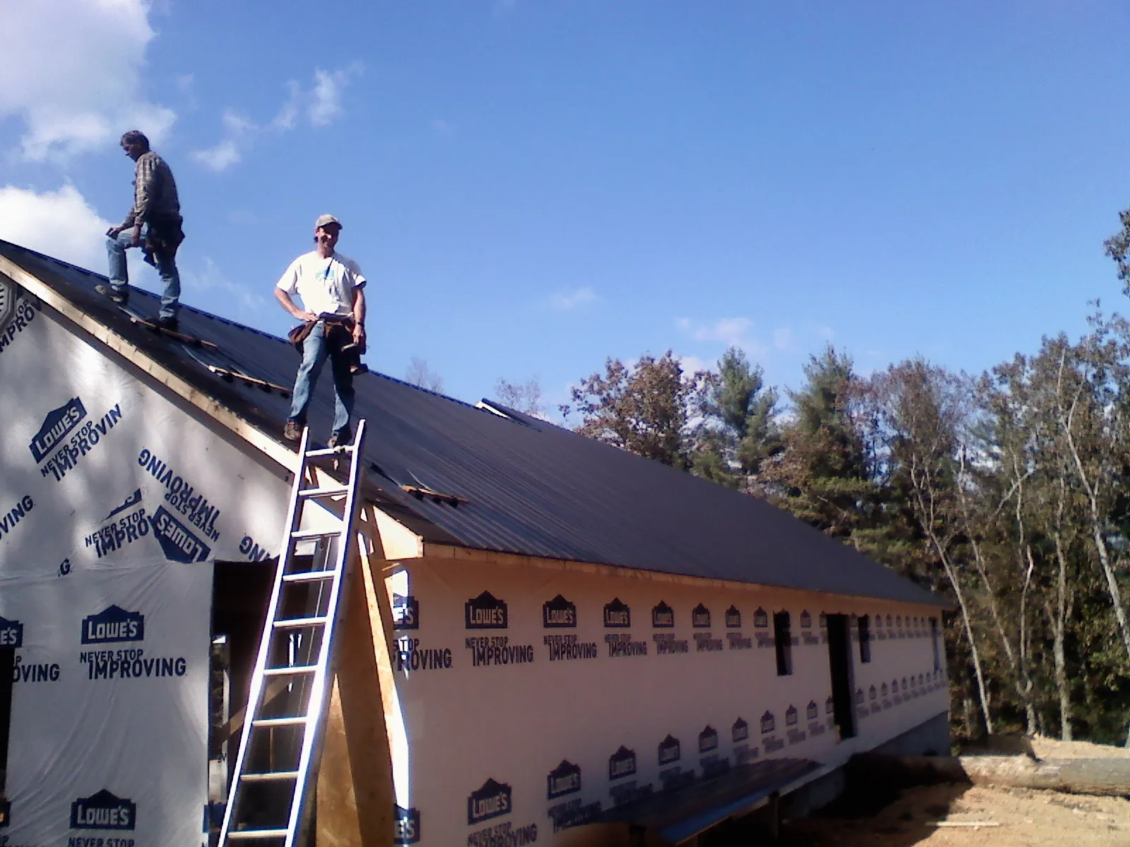 Two roofers standing on a long dark metal roof over a wrapped building in Leiters Ford