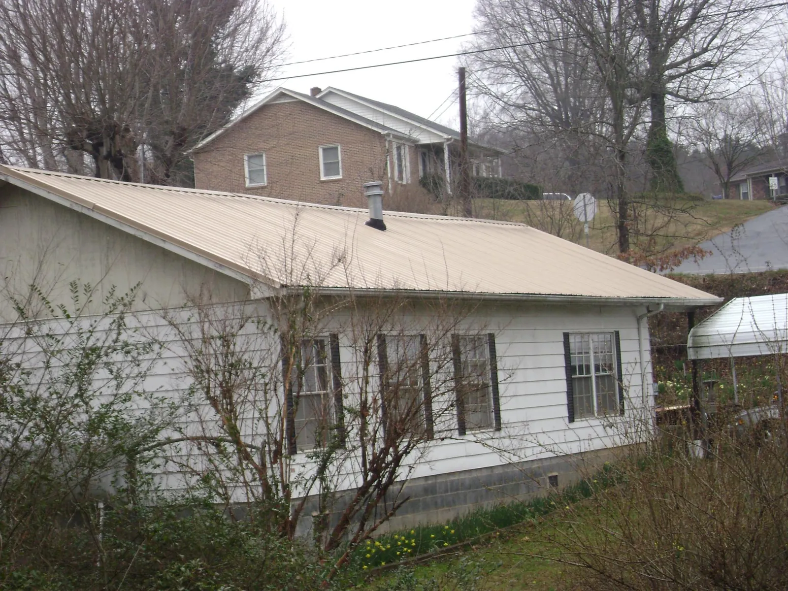 Tan metal roof on a white sided house set into a hillside — Commercial Roofing by Roofing Brothers in Leiters Ford